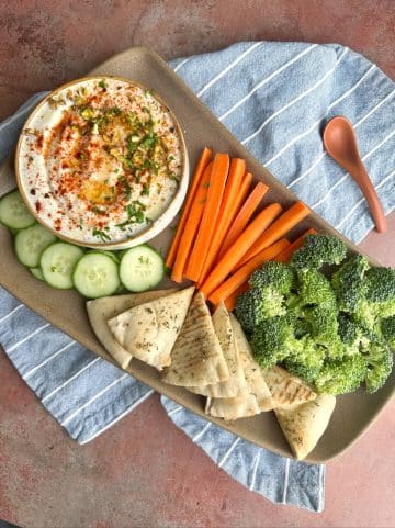 A crudités platter with whipped feta, cucumbers, carrots, broccoli, and pita slices.