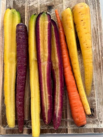 A bunch of rainbow carrots, sliced in half, on a cutting board.