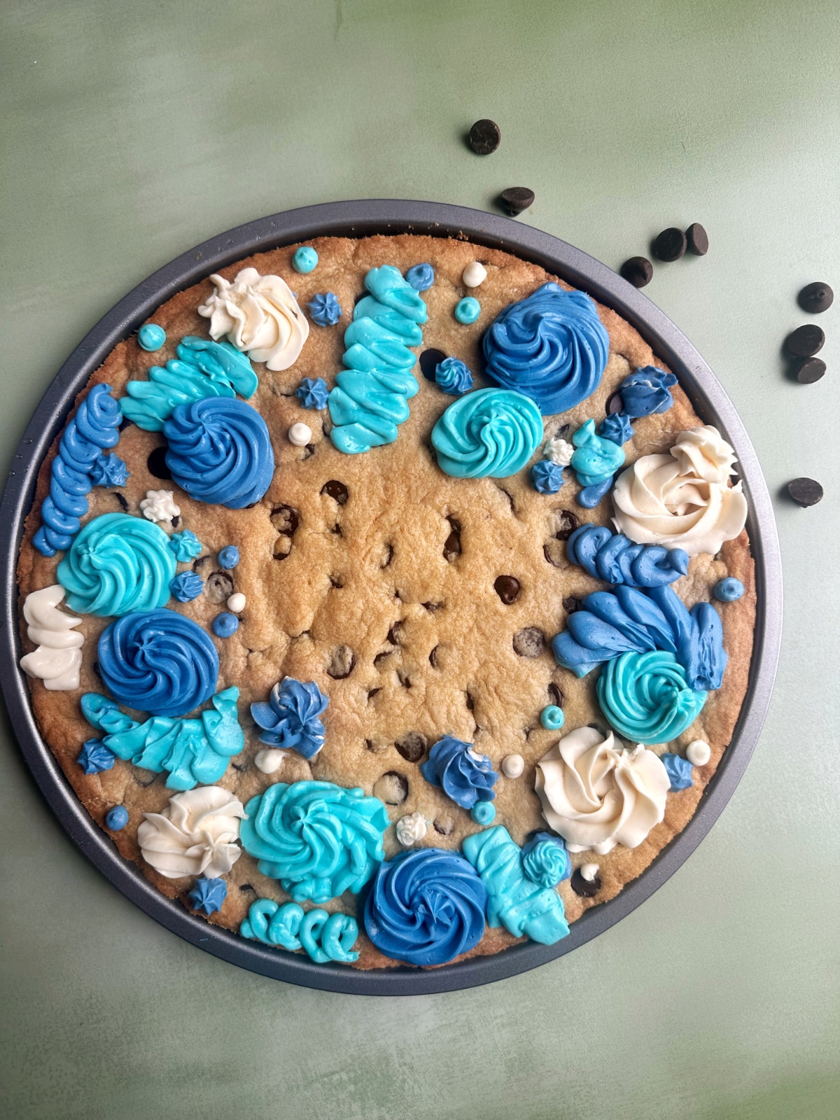 A Cookie Cake with chocolate chips and icing flowers in a round pan.