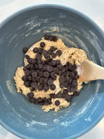 Chocolate chips poured into a mixing bowl filled with cookie dough.