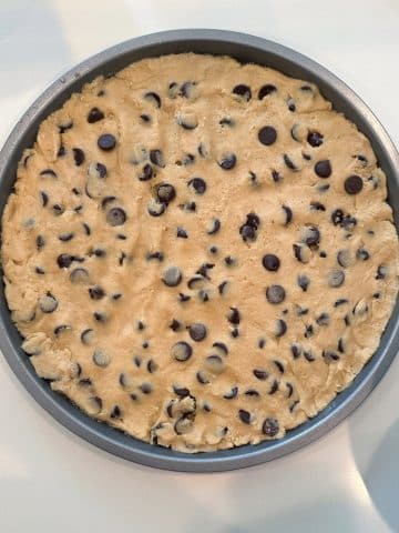 A round pizza pan filled with cookie dough, before being baked.
