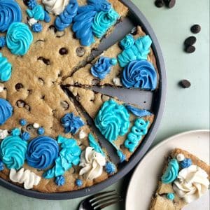 A pan of chocolate chip cookie cake with slices cut out of it, and blue and white icing.