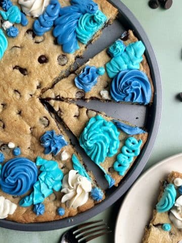 A pan of chocolate chip cookie cake with slices cut out of it, and blue and white icing.