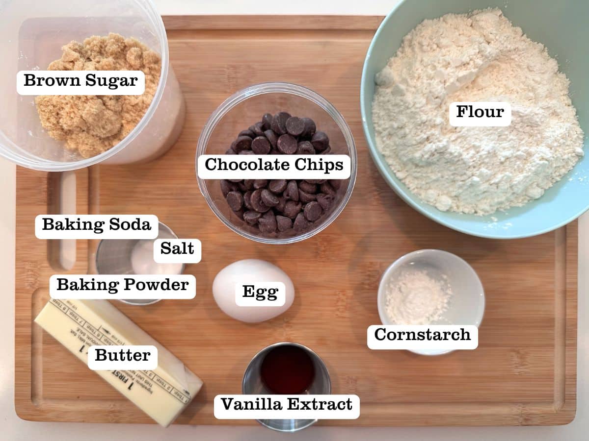 The ingredients for a cookie cake on a wooden board, including bowls of chocolate chips, brown sugar, and flour.