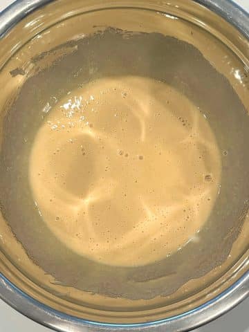 A mixing bowl with a light yellow mixture of whisked eggs and sugar.