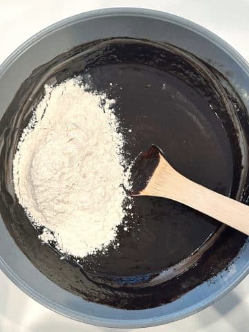 Melted chocolate and butter with flour in a mixing bowl with a wooden spoon.