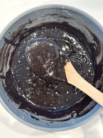 A wooden spoon displaying the texture of brownie batter over the rest of the bowl.