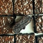 A pan of sliced crinkle top brownies with one turned to the side to show the inside texture.