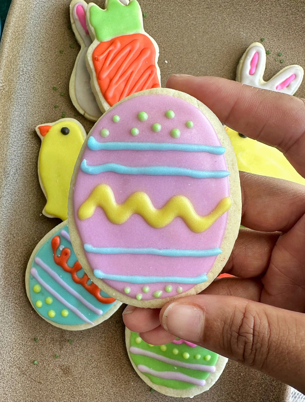A hand holding a sugar cookie decorated like an Easter egg.