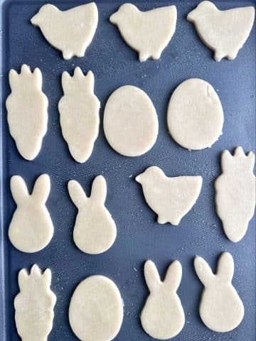 A pan of cut out sugar cookies shaped chicks, carrots, eggs, and rabbits, before being baked.