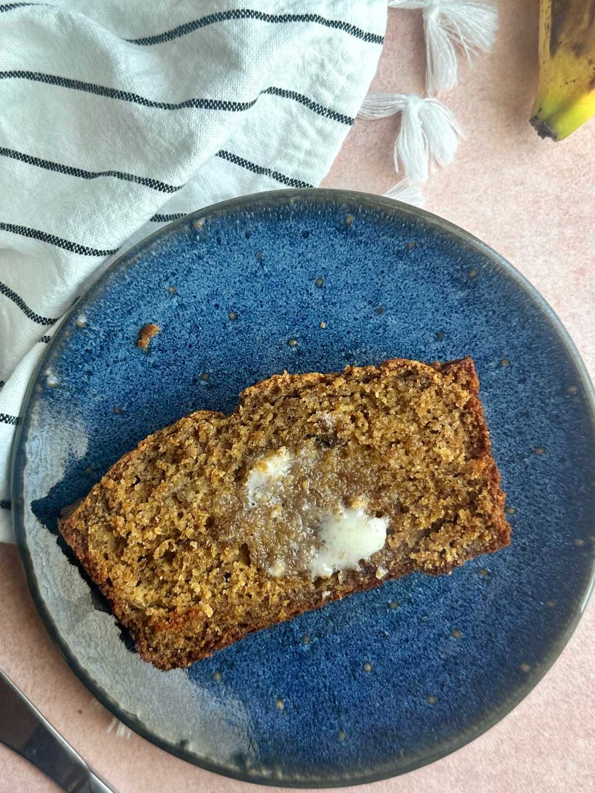 A slice of banana bread with a knob of softened butter on it.