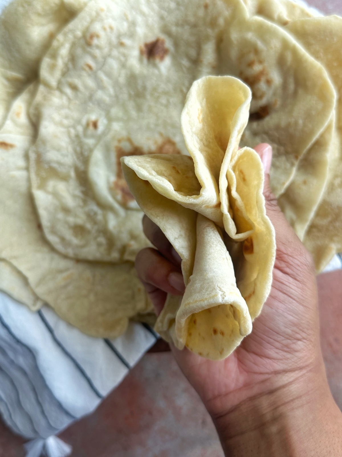 A hand squishing together a homemade flour tortilla to show the pliability.