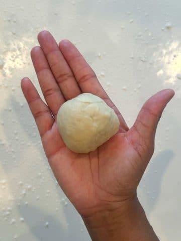 A hand holding a piece of tortilla dough rounded into a ball.