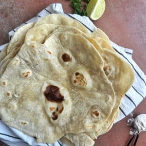 A stack of homemade flour tortillas on a kitchen towel.