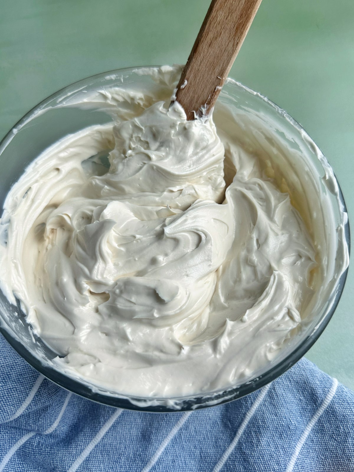 A bowl filled with homemade American buttercream with a silicone spatula sticking out of it.