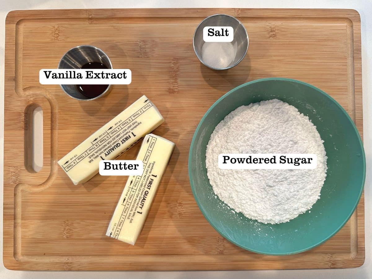 A wooden board containing ingredients for American buttercream including butter, bowls of powdered sugar, salt, and vanilla extract.