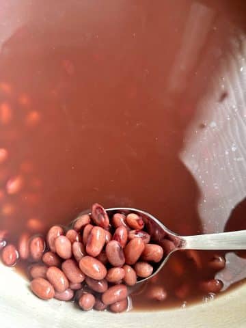A spoon scooping up red beans from their red soaking liquid.
