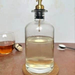 A glass pouring bottle filled with a clear liquid of simple syrup.