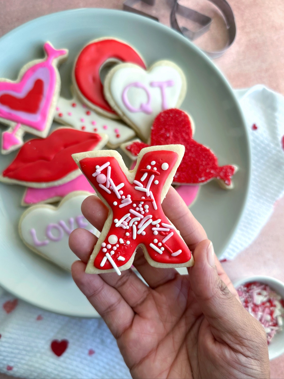 A hand holding an X-shaped cut out cookie decorated in a Valentine's Day theme.