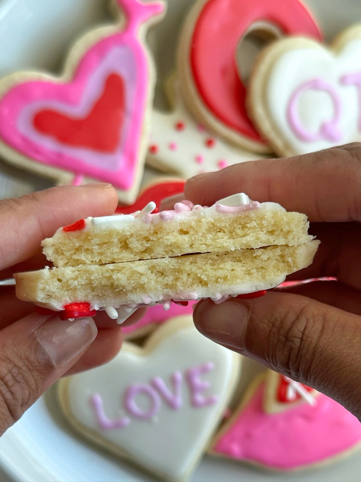 Two hands holding a heart-shaped cut out cookie broken in half, to show the interior texture.
