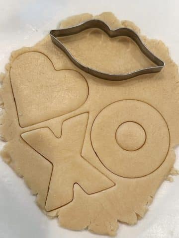 Cookie dough rolled out into a thin layer with Valentine's Day shapes cut into the dough.
