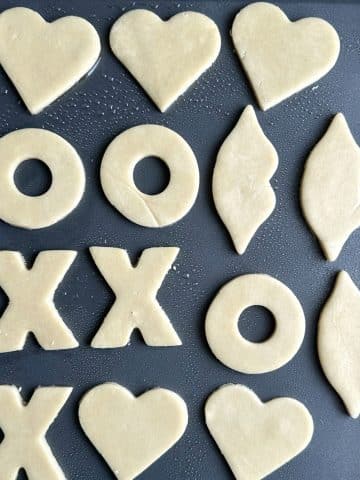 A pan of cut out sugar cookies shaped as hearts, X's and O's, and lops, before being baked.