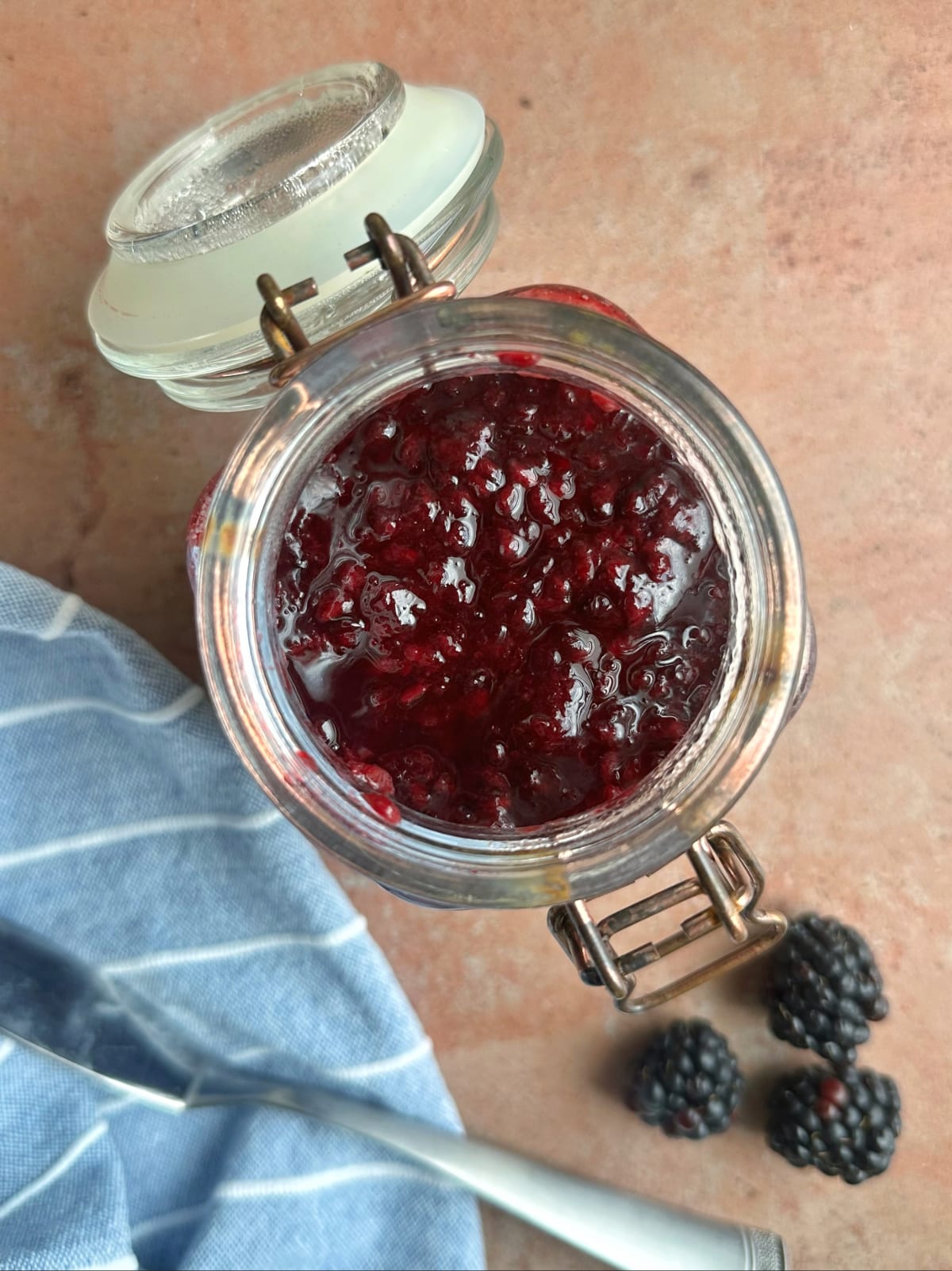 A jar of blackberry preserves with more berries on the side.