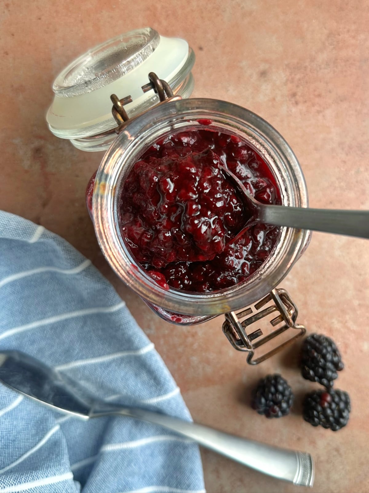 A glass canning jar filled with blackberry preserves and a spoon sticking out.