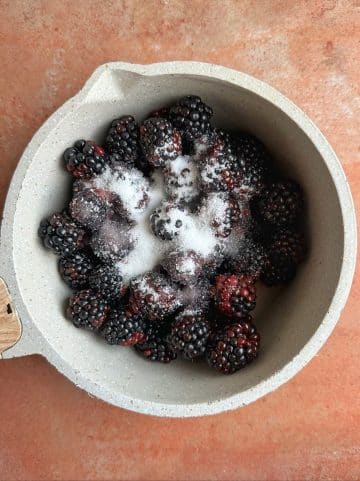 A pot filled with fresh blackberries and white sugar on top.