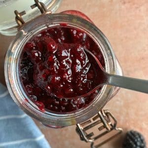 A glass jar containing blackberry jam with a spoon sticking out of it.