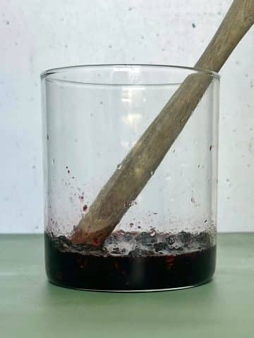 Muddled blackberries and mint leaves in a tall, clear glass.
