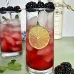 A glass of blackberry mojito with lime slices and fresh berries for garnish.