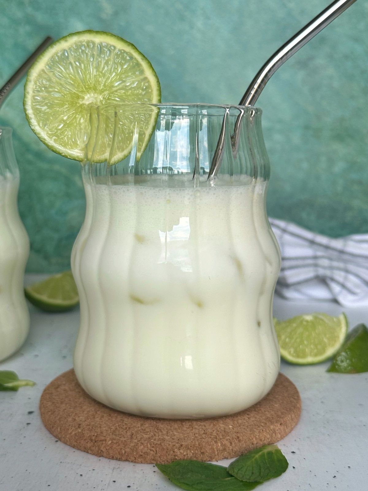 A glass of limeade over ice, with a metal straw.