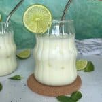 A glass of Brazilian lemonade with a lime wedge on the side of the cup, plus a metal straw sticking out.