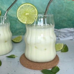 A glass of Brazilian lemonade with a lime wedge on the side of the cup, plus a metal straw sticking out.