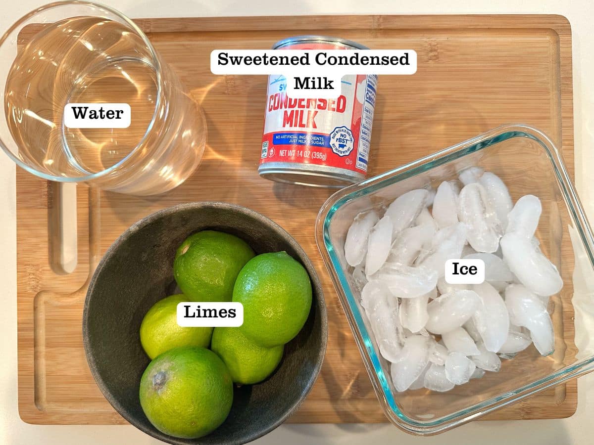 A wooden board with containers of limes, water, ice, and a can of condensed milk.