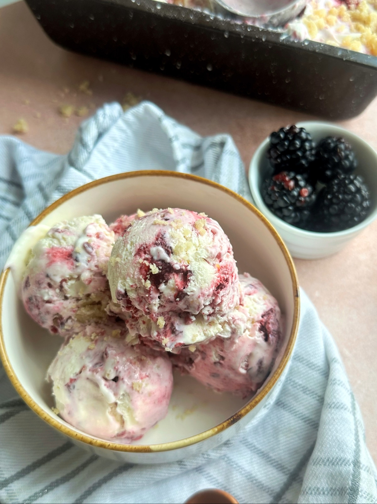 Five scoops of lemon blackberry swirl ice cream in a cream-colored bowl with more berries on the side.