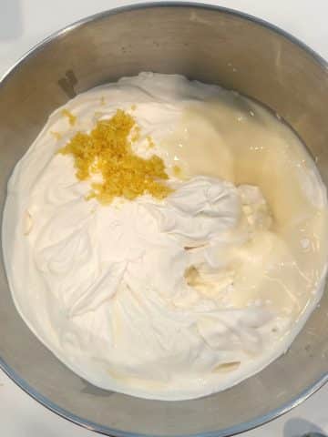 A mixing bowl filled with whipped cream, lemon zest, lemon juice, and sweetened condensed milk.