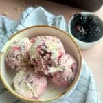 A bowl filled with scoops of Lemon Blackberry Ice Cream with another container of berries on the side.