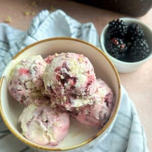 A bowl filled with scoops of Lemon Blackberry Ice Cream with another container of berries on the side.