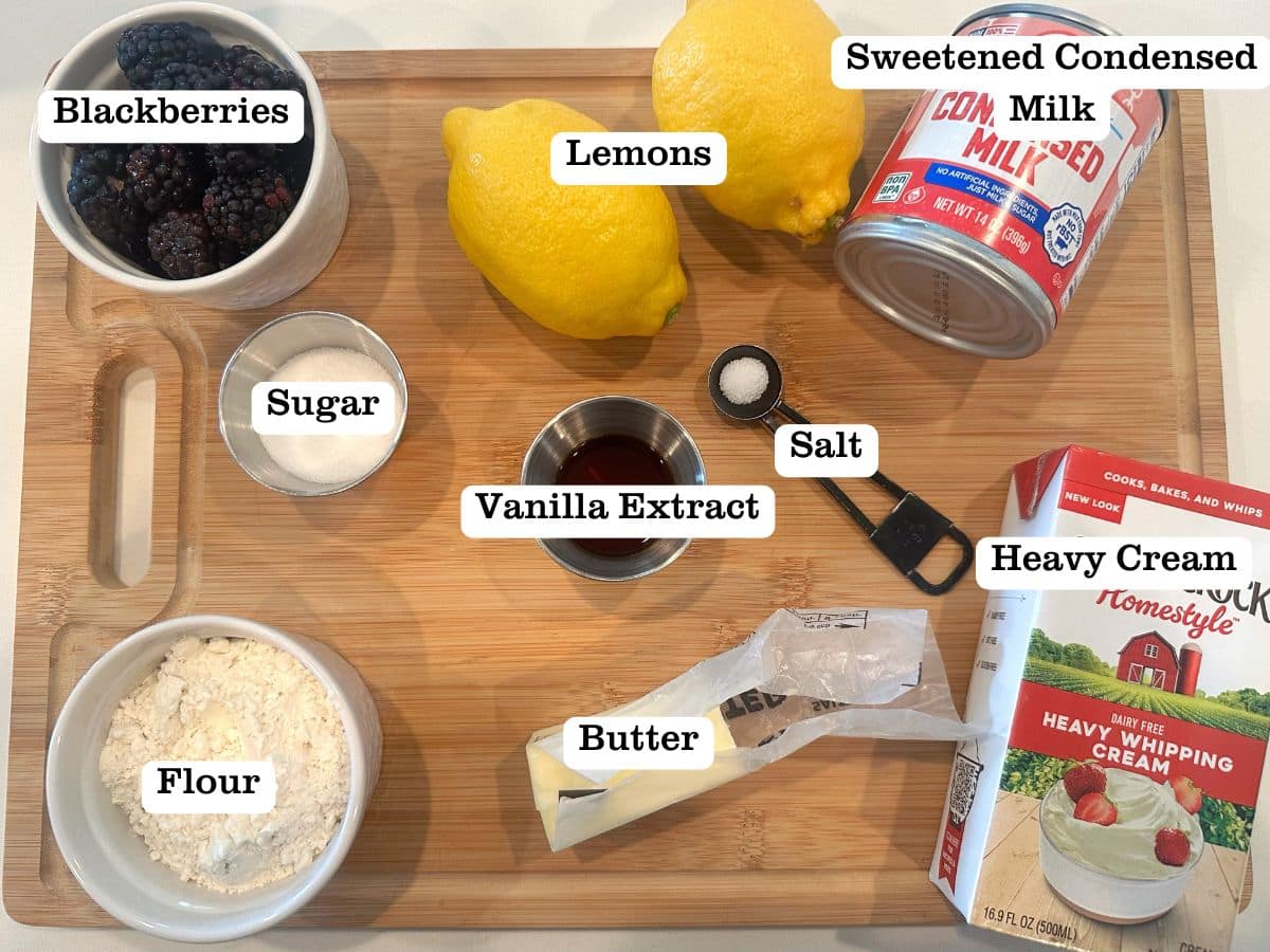 A wooden board containing ice cream ingredients, including bowls of blackberries, sugar, and vanilla extract.