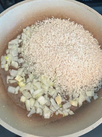 Onions and white rice in a pan with oil.