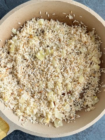 Toasted rice and onions in a cream-colored skillet.