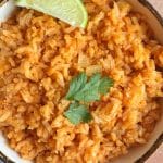 A bowl of Mexican red rice with a lime quarter and a few sprigs of cilantro.