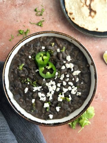 A bowl of mashed black beans with crumbled white cheese and sliced jalapeños on top.