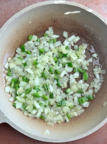 A pan filled with chopped onion and jalapeno, being sautéed in oil.
