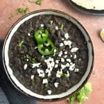 A bowl of refried black beans with sliced jalapeños and cotija cheese on top.
