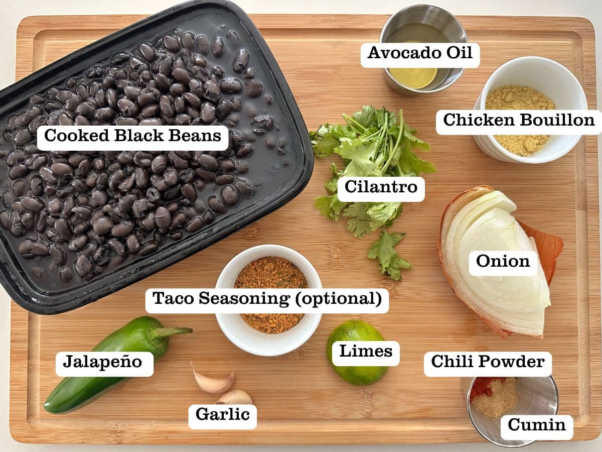 A wooden board containing bowls of ingredients for refried black beans, including cooked beans, onion, jalapeño, and chicken bouillon.