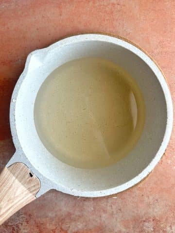A cream-colored pot showing simple syrup after melting over the heat.
