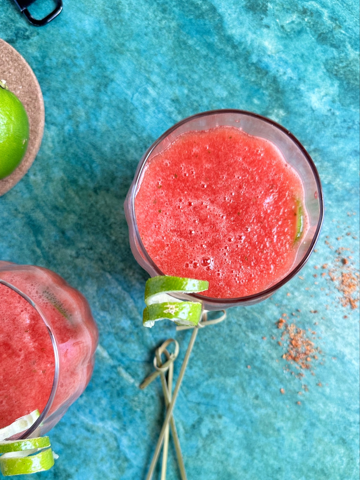 A glass of watermelon refresher mocktail with whole limes on the side.